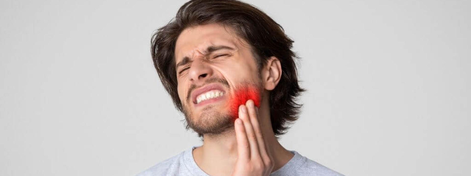 Young man with a toothache and tooth infection holding his jaw in pain